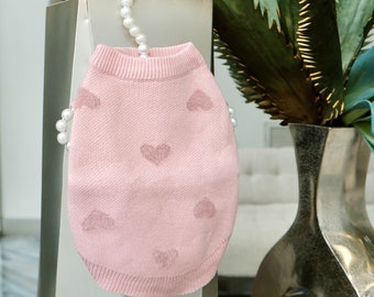May include: A pink knitted sweater for a pet with a heart pattern.