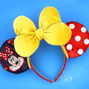 May include: A Minnie Mouse-themed headband with a large yellow bow and two round ears. One ear is red with white polka dots, the other is black with a Minnie Mouse design. The headband is red with gold rope accents.