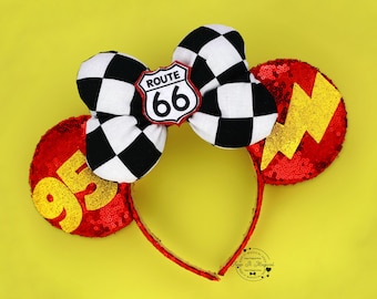 May include: A red sequined headband with a black and white checkered bow, a Route 66 sign, and two ear-shaped embellishments. One ear has a gold lightning bolt, the other has the number 95 in gold.
