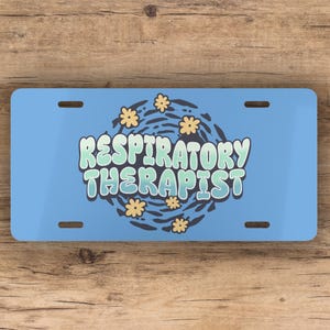 May include: Blue and white license plate with the text "Respiratory Therapist" in a stylized font with a swirl design and yellow flowers.