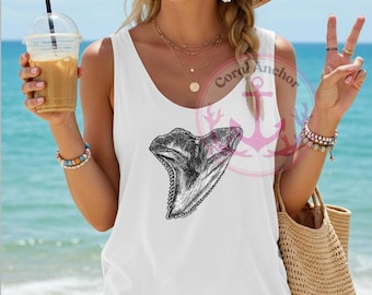 May include: White tank top with a black and white graphic of a shark tooth. The tank top has a scoop neck and is worn by a person on a beach. The words "Coral Anchor" are printed on the shirt.
