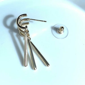 May include: Gold-toned hoop earrings with three dangling, thin, gold-toned bars.