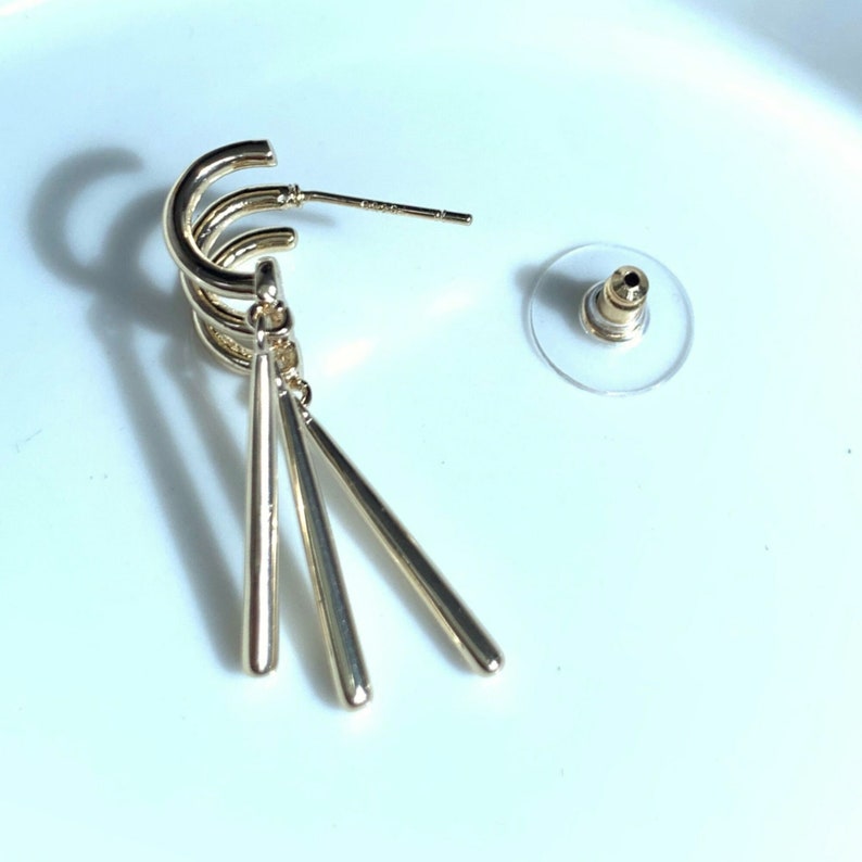 May include: Gold-toned hoop earrings with three dangling, thin, gold-toned bars.