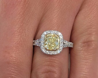 May include: A gold engagement ring with a large, cushion-cut yellow diamond surrounded by smaller diamonds. The ring is set in white gold and has a delicate band.