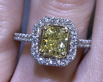 May include: A yellow diamond engagement ring with a halo setting. The ring is set in white gold and features a square-shaped diamond with smaller diamonds surrounding it.