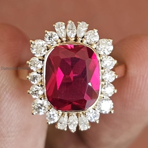 Puede incluir: Un anillo de oro con una gran piedra preciosa rectangular roja rodeada de piedras preciosas más pequeñas y transparentes.