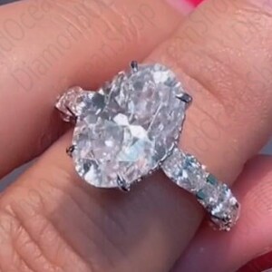 Op de afbeelding: Een zilveren verlovingsring met een grote ovale diamant en kleinere diamanten die in de band zijn gezet.