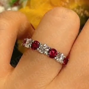 May include: A silver band ring with a row of red gemstones and smaller clear gemstones.