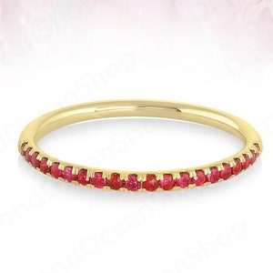 May include: A thin gold band ring with a row of small red gemstones around the entire band.