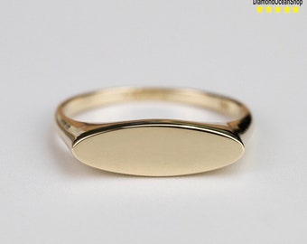 May include: A gold signet ring with a smooth, oval-shaped top. The ring is simple and elegant.