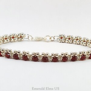 May include: A silver and red beaded bracelet with a silver clasp. The bracelet is made with small, round beads and features a repeating pattern of red and silver beads.