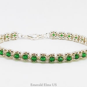 May include: A silver and green beaded bracelet with a silver clasp. The bracelet is made with small, round beads and features a row of green beads.