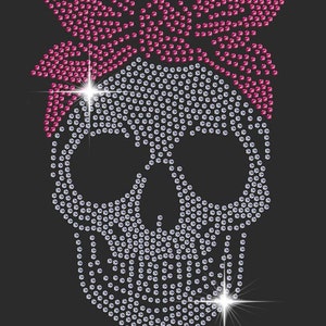May include: A rhinestone skull design with a pink rhinestone bandana. The skull is made of clear rhinestones and the bandana is made of pink rhinestones.
