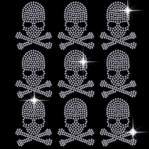 May include: Nine silver skull and crossbones designs made of rhinestones. The skulls are all facing forward with the crossbones behind them.