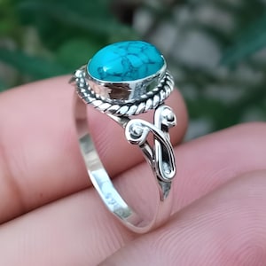 Może przedstawiać: Srebrny pierścionek z owalnym turkusem. Pierścionek ma szczegółowy wzór wokół kamienia i na obrączce. Tekst "Silver Jewellery Exports" jest widoczny na dole obrazu.