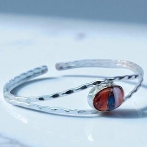 Könnte beinhalten: Silberner Armreif mit gehämmertem Muster und einem ovalen, mehrfarbigen Stein. Der Stein hat Farbtöne von Rot, Orange, Blau und Weiß. Der Text "SILVER JEWELLERY EXPORTS" befindet sich unten.