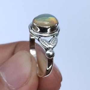 Op de afbeelding: Een zilveren ring met een ovale opaal edelsteen. De opaal heeft gele, oranje en groene tinten. De ring heeft een bladeren ontwerp op de band. De tekst "SILVER JEWELLERY EXPORTS" is zichtbaar.