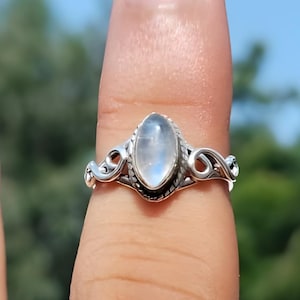 May include: A silver ring with an oval, light blue gemstone. The ring has a decorative, swirling design on the band. The text "Silver Jewellery Exports" is visible at the bottom of the image.