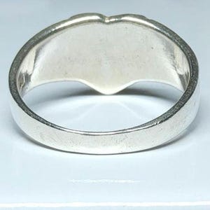 Puede incluir: Un anillo de plata con un dise&ntilde;o en forma de coraz&oacute;n. El anillo tiene una banda ancha y una superficie lisa y pulida. La forma de coraz&oacute;n es visible en la parte superior del anillo.