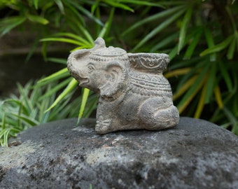 May include: A gray stone elephant figurine with intricate details, sitting on a rock. The elephant has a small pot on its back.