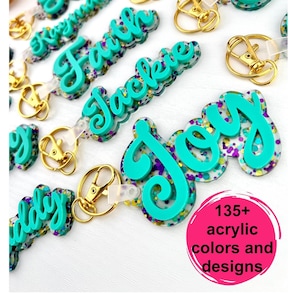 May include: Teal blue acrylic keychains with glitter and personalized names.  The keychains have gold split rings and clear plastic straps.  135+ acrylic colors and designs.