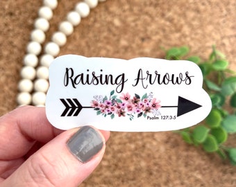 May include: White sticker with black text that reads "Raising Arrows" and a black arrow with pink flowers. The text "Psalm 127:3-5" is below the arrow.