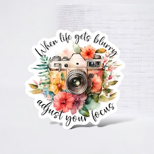 May include: A vintage camera with a floral design and the text "When life gets blurry adjust your focus".
