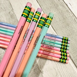 Puede incluir: Un conjunto de l&aacute;pices de colores pastel con detalles verdes y amarillos. Cada l&aacute;piz est&aacute; inscrito con un nombre y una frase inspiradora como "I AM WORTHY" o "I AM STRONG". L&aacute;pices adicionales est&aacute;n etiquetados como "Mrs. Cunningham's class".