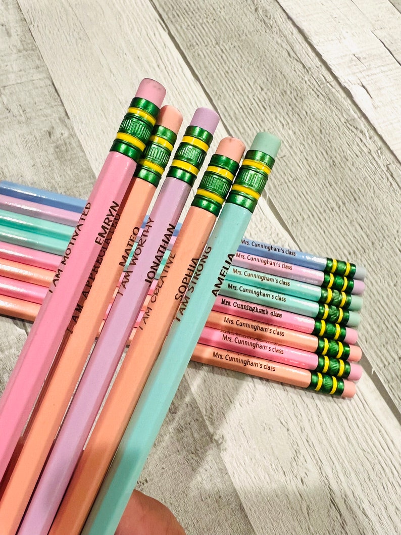 Puede incluir: Un conjunto de l&aacute;pices de colores pastel con detalles verdes y amarillos. Cada l&aacute;piz est&aacute; inscrito con un nombre y una frase inspiradora como "I AM WORTHY" o "I AM STRONG". L&aacute;pices adicionales est&aacute;n etiquetados como "Mrs. Cunningham's class".