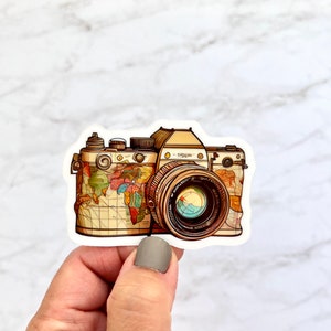 May include: A vintage camera sticker with a world map design. The camera is brown and has a black lens. The sticker is white with a black outline.