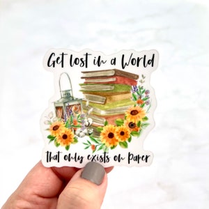 May include: A sticker with a stack of books, a lantern, and sunflowers. The text reads "Get lost in a world that only exists on paper."