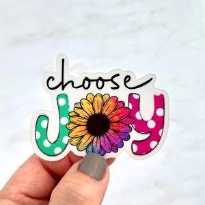 May include: A white sticker with the words "choose joy" in black script. The word "joy" is decorated with a colorful sunflower and polka dots.