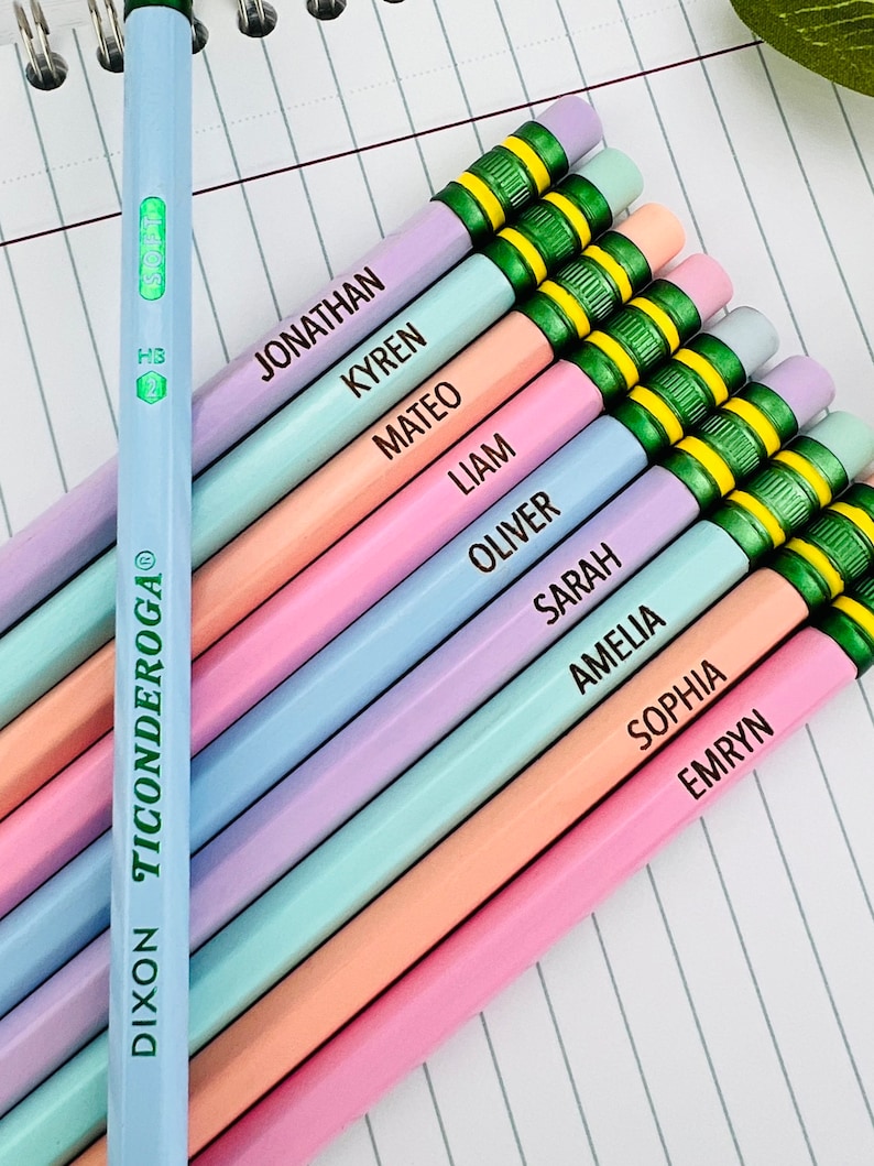 Puede incluir: Una colecci&oacute;n de l&aacute;pices de colores pastel, cada uno con un nombre impreso en el lateral. Los l&aacute;pices est&aacute;n dispuestos en diagonal sobre un cuaderno rayado. Un l&aacute;piz es de color azul claro con el texto "Dixon Ticonderoga". Los l&aacute;pices tienen detalles verdes y amarillos.