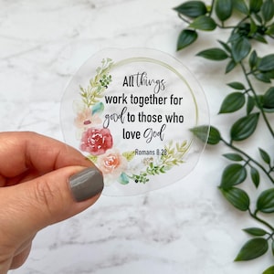 May include: A clear sticker with a floral wreath design and the text "All things work together for good to those who love God" with the scripture reference "Romans 8:28".