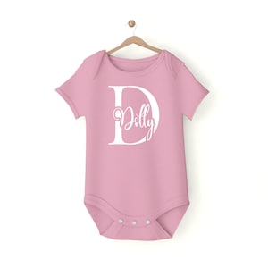 May include: A pink baby onesie with a white letter D and the name "Dolly" inside the letter.