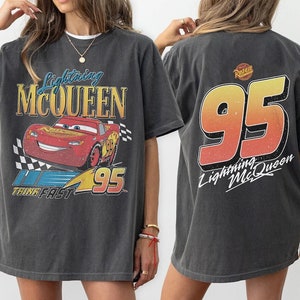 Pu&ograve; includere: Una maglietta grigia oversize con una grafica in stile vintage di Saetta McQueen dal film Cars della Disney Pixar. La parte anteriore della maglietta presenta un'auto da corsa rossa con il testo "Lightning McQueen" e "Think Fast" e il numero "95". La parte posteriore della maglietta presenta il numero "95" in un gradiente rosso, arancione e giallo con il testo "Lightning McQueen".