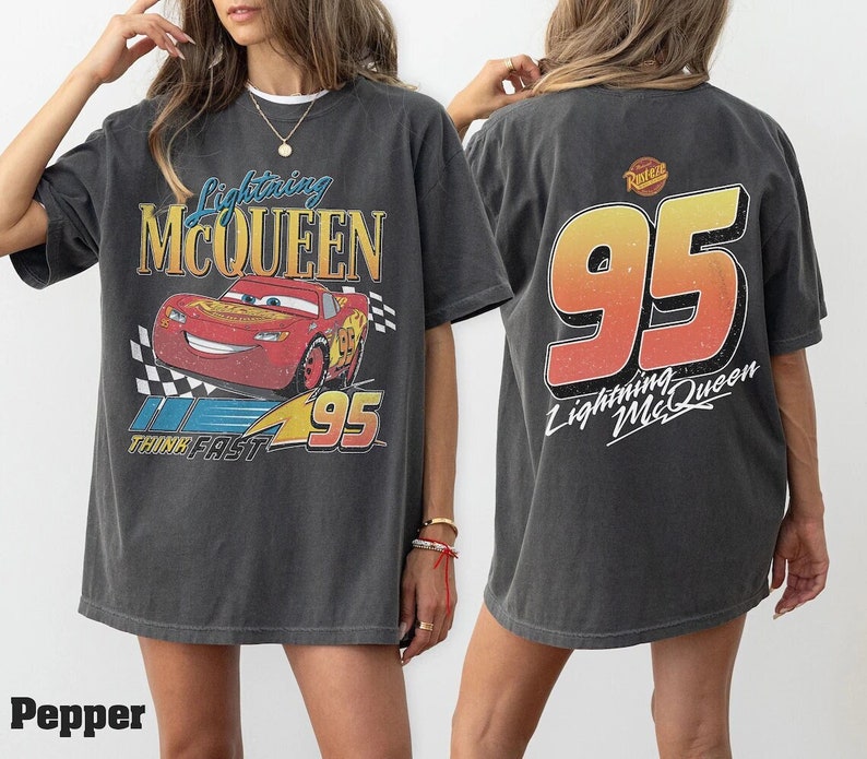 Pu&ograve; includere: Una maglietta grigia oversize con una grafica in stile vintage di Saetta McQueen dal film Cars della Disney Pixar. La parte anteriore della maglietta presenta un'auto da corsa rossa con il testo "Lightning McQueen" e "Think Fast" e il numero "95". La parte posteriore della maglietta presenta il numero "95" in un gradiente rosso, arancione e giallo con il testo "Lightning McQueen".