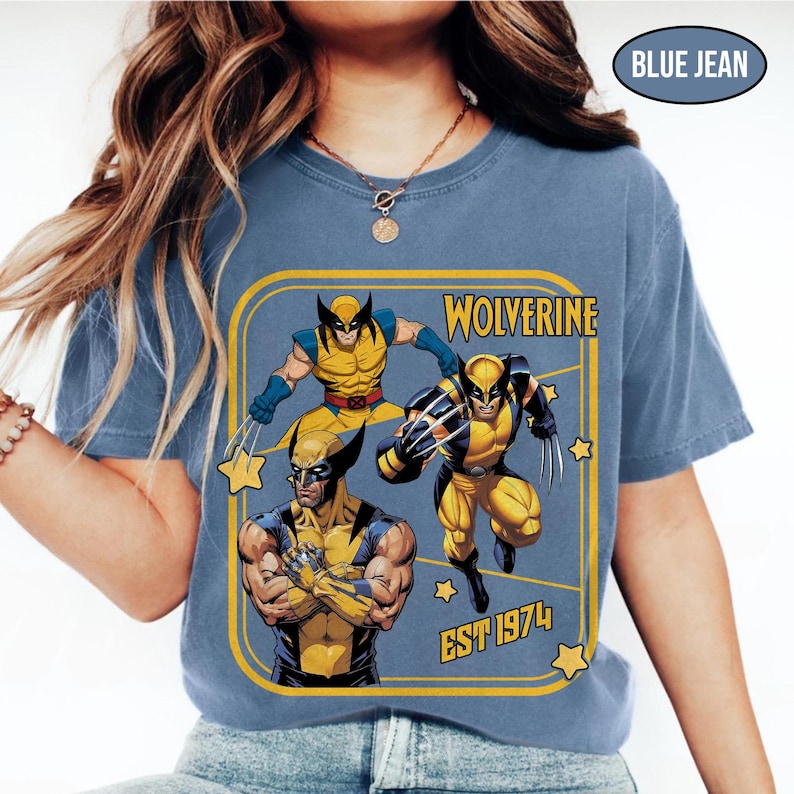 Puede incluir: Camiseta azul vaquero con un gr&aacute;fico de Wolverine. El gr&aacute;fico incluye tres ilustraciones de Wolverine en amarillo y azul, con la palabra "Wolverine" y "EST 1974" en texto amarillo. La camiseta tiene cuello redondo.