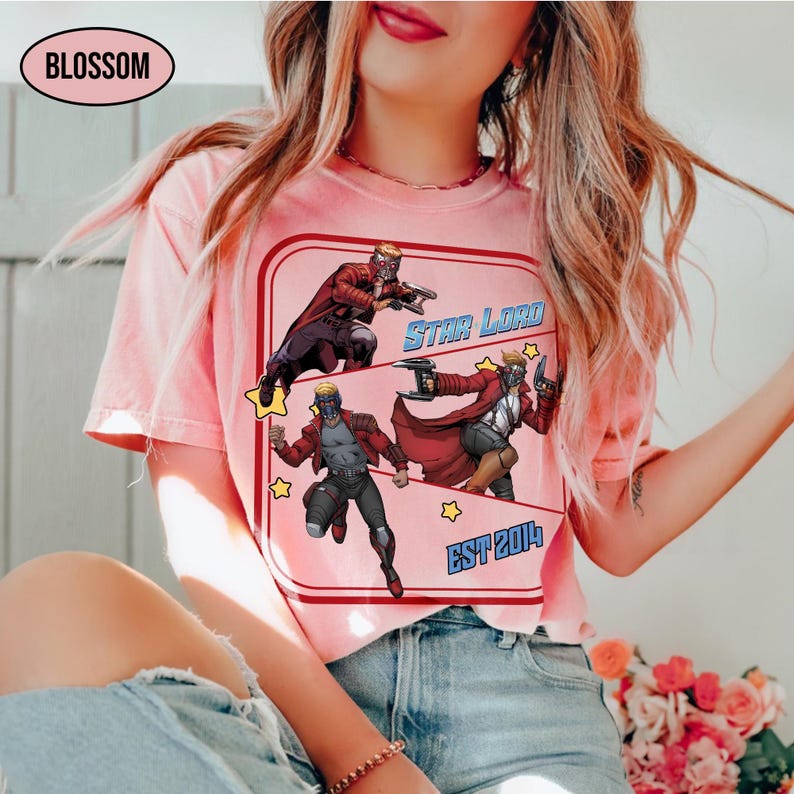 Puede incluir: Camiseta rosa claro con un gr&aacute;fico de Star Lord. El gr&aacute;fico incluye ilustraciones de Star Lord en poses de acci&oacute;n, las palabras "STAR LORD" y "EST 2014" en un estilo retro. La camiseta tiene cuello redondo.