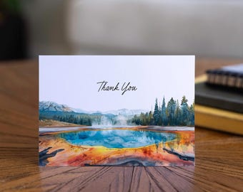 May include: A greeting card featuring a watercolour painting of a vibrant hot spring in a natural setting. The card shows a blue and orange hot spring with mountains and trees. The words "Thank You" are written in cursive script.