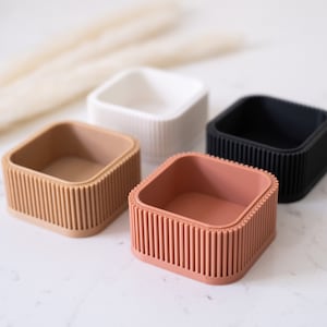 May include: Four square-shaped containers with ribbed edges. The containers are in white, beige, coral, and black.