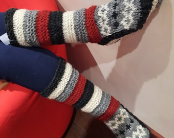 May include: Knee-high knitted socks with a geometric pattern on the foot and stripes of red, black, gray, and white. The socks are thick and appear warm, suitable for cold weather.