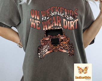 Peut inclure: Un t-shirt gris avec le texte "On Weekends We Wear Dirt" dans une police d'écriture marron et léopard. Un quad marron et léopard se trouve sous le texte. Le texte "IndicaChic Designs" se trouve dans le coin inférieur droit de l'image.