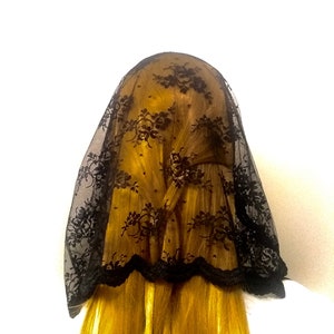 May include: Black lace veil with a scalloped edge. The veil is made of delicate lace and has a floral pattern.