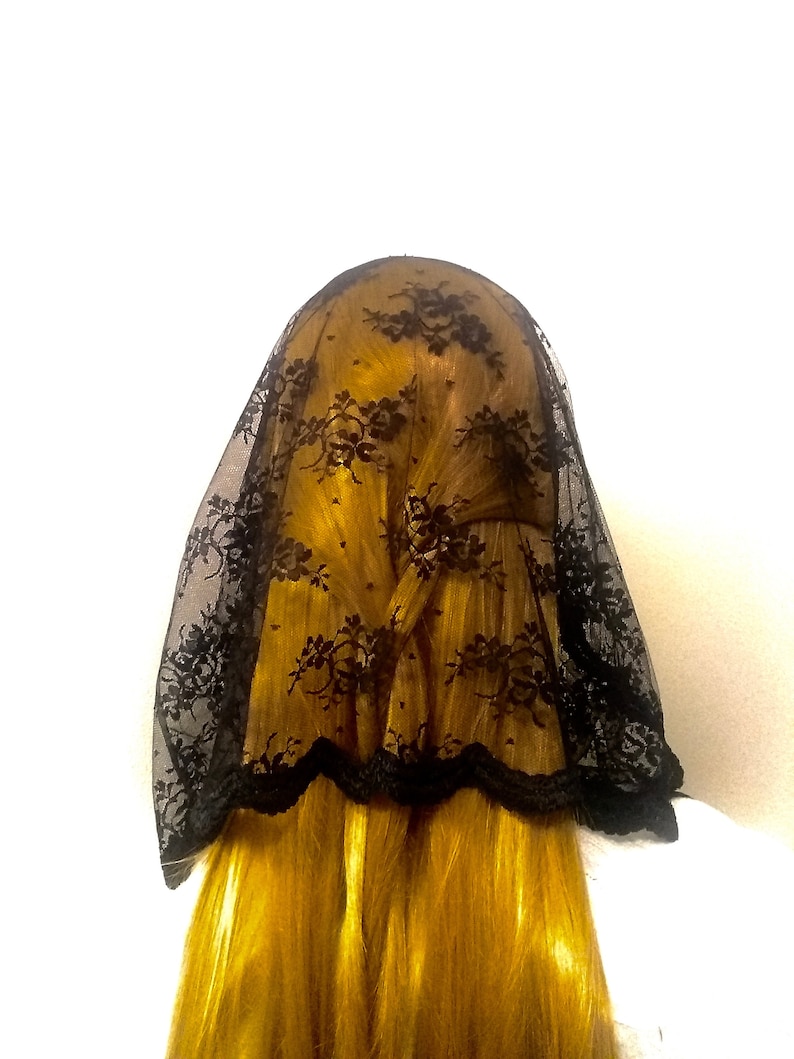 May include: Black lace veil with a scalloped edge. The veil is made of delicate lace and has a floral pattern.