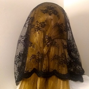 May include: Black lace veil with a scalloped edge. The veil is worn over a person's head and hair.