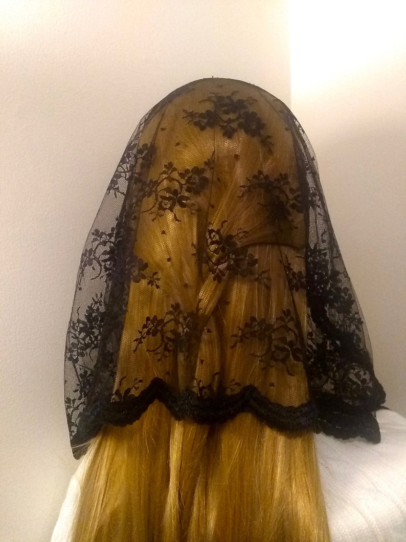 May include: Black lace veil with a scalloped edge. The veil is worn over a person's head and hair.