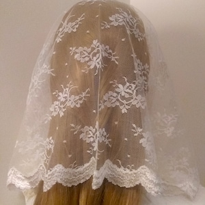 May include: White lace veil with a scalloped edge. The veil is made of a delicate, sheer fabric and has a floral pattern.