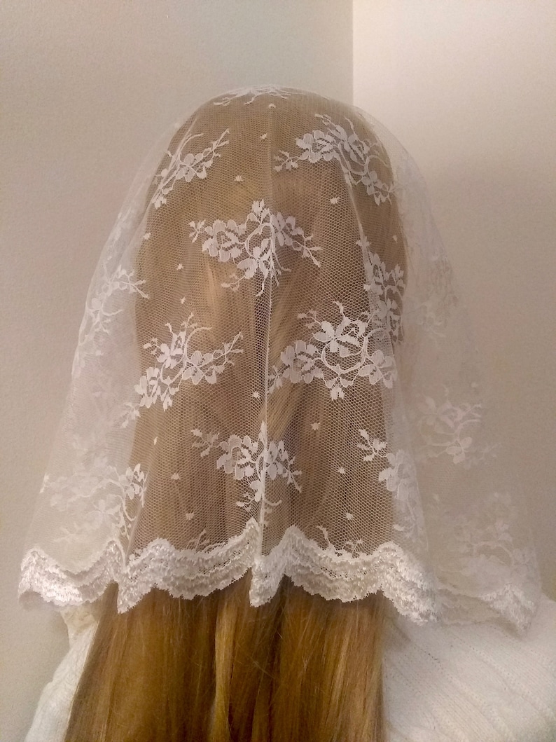 May include: White lace veil with a scalloped edge. The veil is made of a delicate, sheer fabric and has a floral pattern.