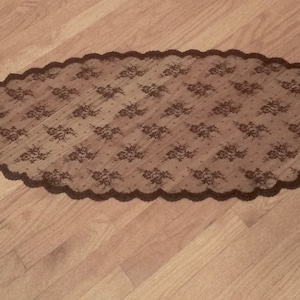 May include: A brown lace table runner with a scalloped edge. The lace has a floral pattern.